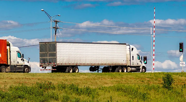 Red and white semi trailer trucks at green light