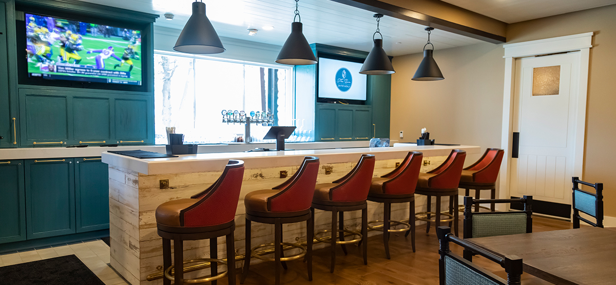 carousel-amenities-cafe-6-bar-1200x556 The Inn library cafe bar seating area with beer on tap and two tv screens.