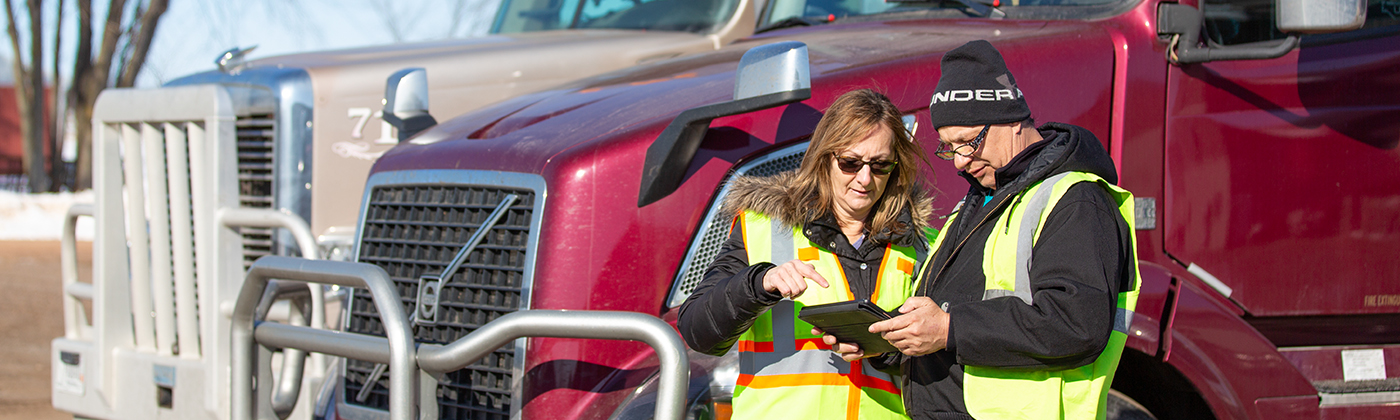 Two drivers look at tablet near their trailer trucks