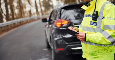 Police officer writing on clipboard behind parked car
