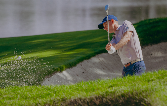 Male golfer hitting his ball out of a sand trap.