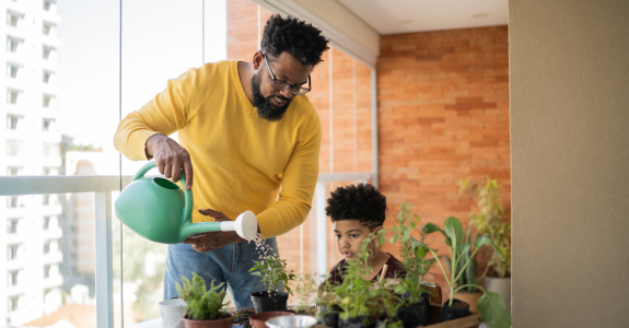 a man and young boy watering plants outside on a balcony