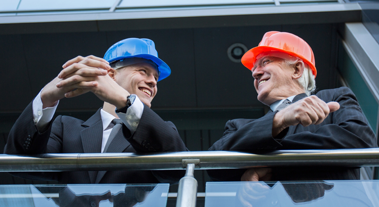 Two business men in suits and hard hats smiling