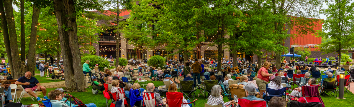 Outdoor concert at SentryWorld with a band performing for a seated audience on a grassy lawn.