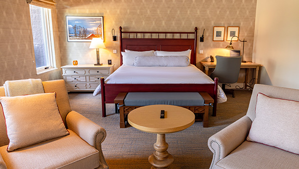 Bedroom with two chairs and a king size bed with a red bed frame. 