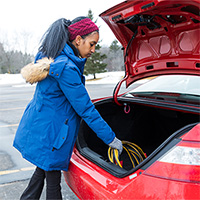 Woman retrieving jumper cables from the trunk of her car.