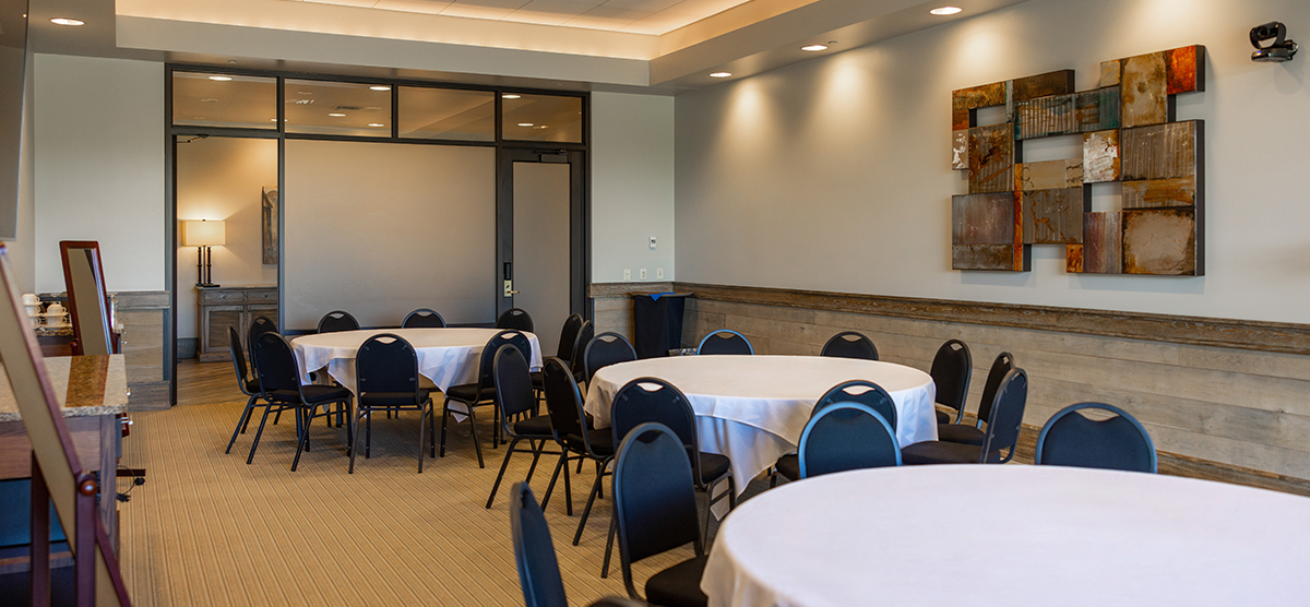 carousel-wedding-venue-community-room-2-1200x556 Room with three round tables with chairs.