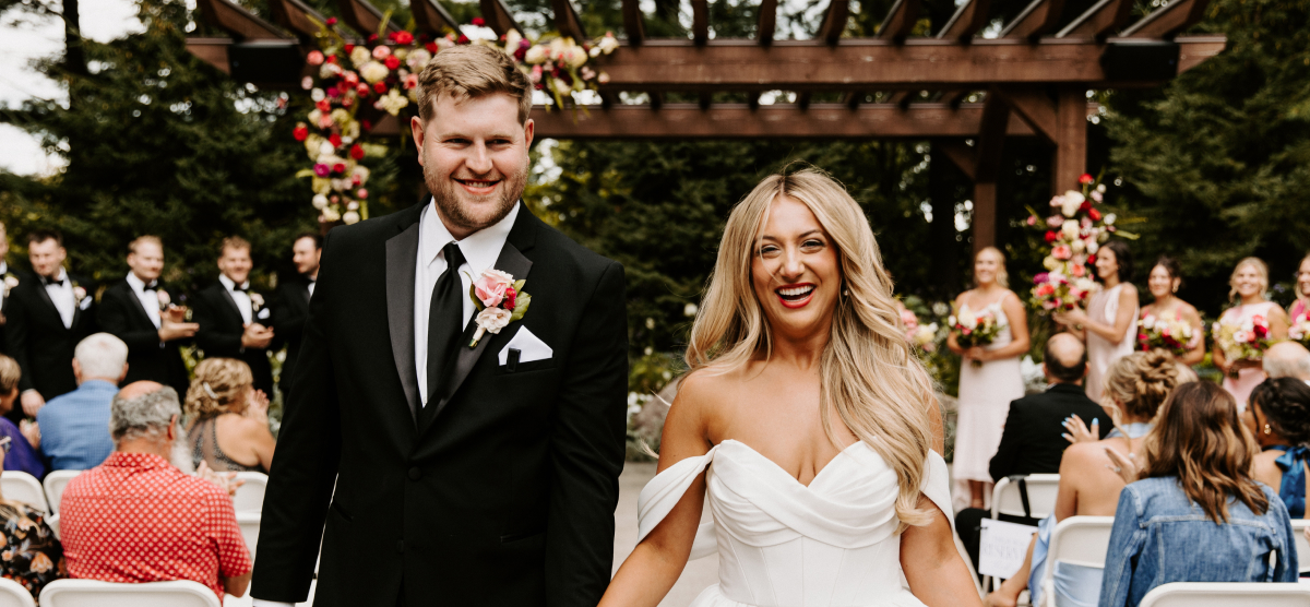Smiling bride and groom walk down the aisle after their outdoor wedding ceremony.