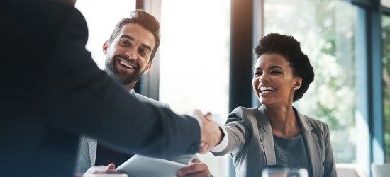 Two business people shaking hands, with a smiling colleague in the background.