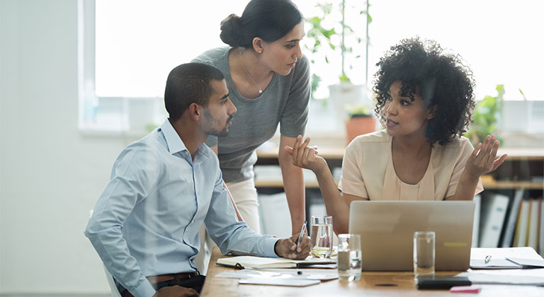 Three people around a laptop in discussion