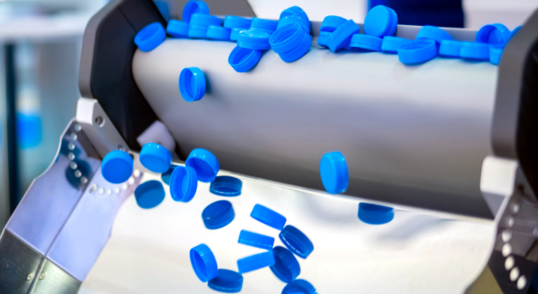 Blue plastic bottle caps moving on a conveyor belt in a factory setting.