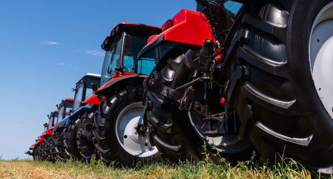 Row of red and blue tractors with large tires, parked in a field under a clear blue sky.
