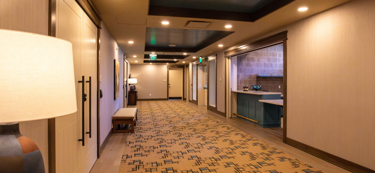 A well-lit hallway with patterned carpet, a bar area, and several doors leading off it.