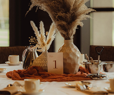 Two vases filled with feathers and a table number card for a wedding reception