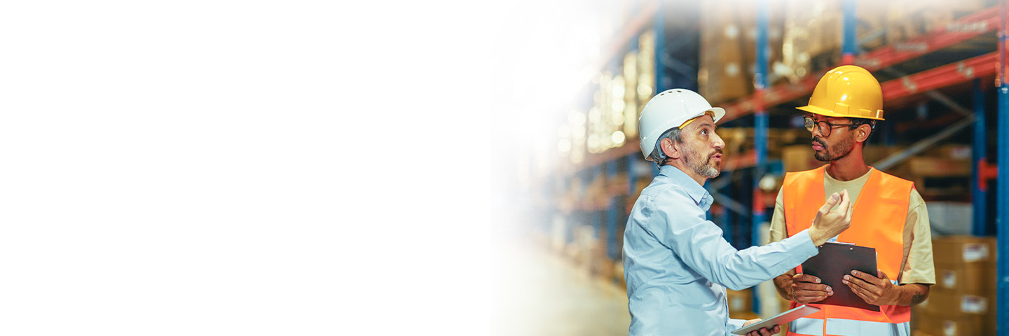 Business professional and warehouse employee wearing hard hats talking