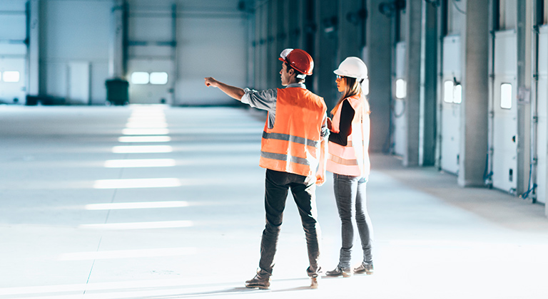 Two people in safety gear planning in warehouse