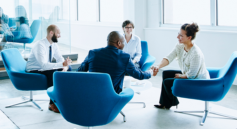 Business professionals in a modern office lounge, with two people shaking hands.