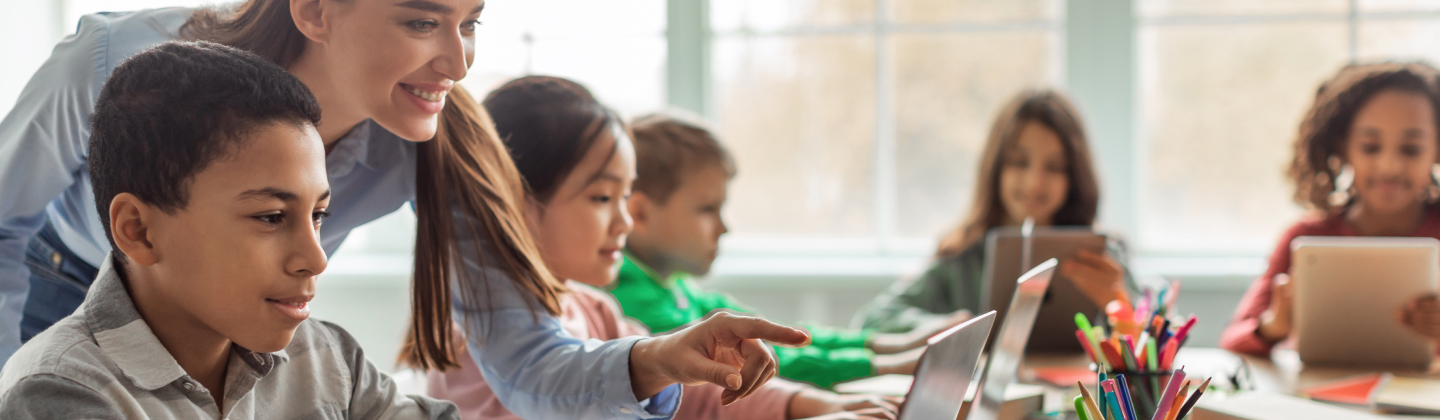 Teacher helps students learn on laptops in a bright classroom.