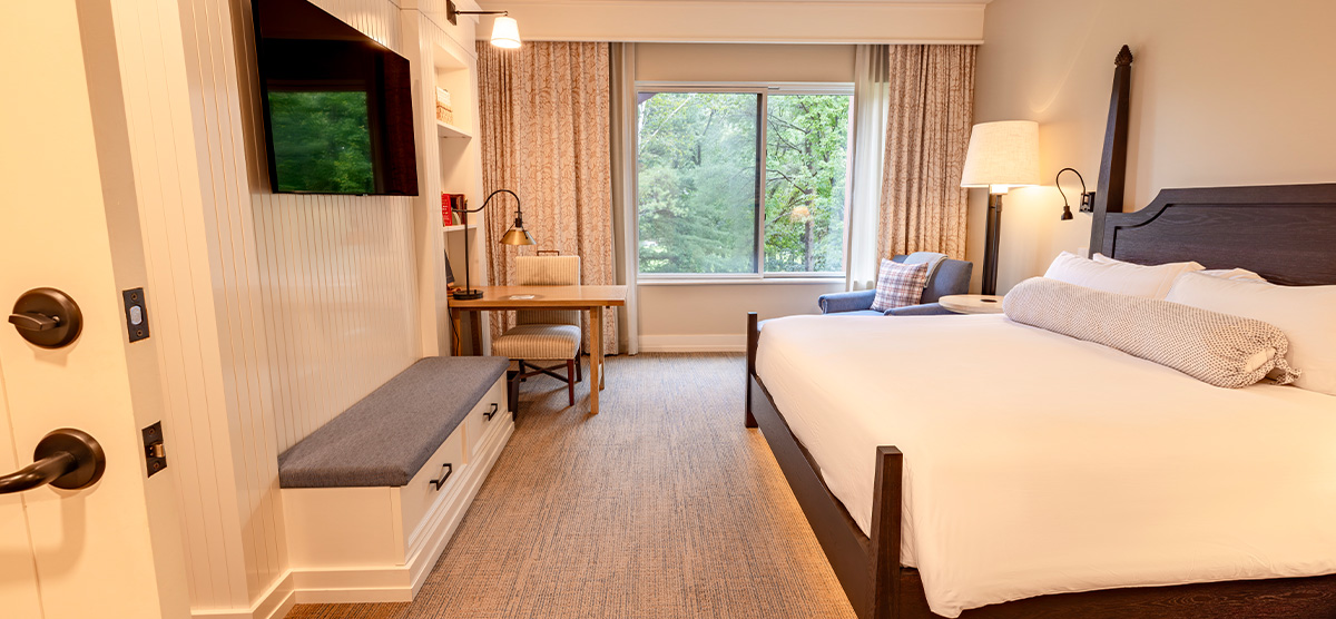 carousel-executive-king-suite-1br-4-1200x556 King bed with a chair, ottoman and a desk.