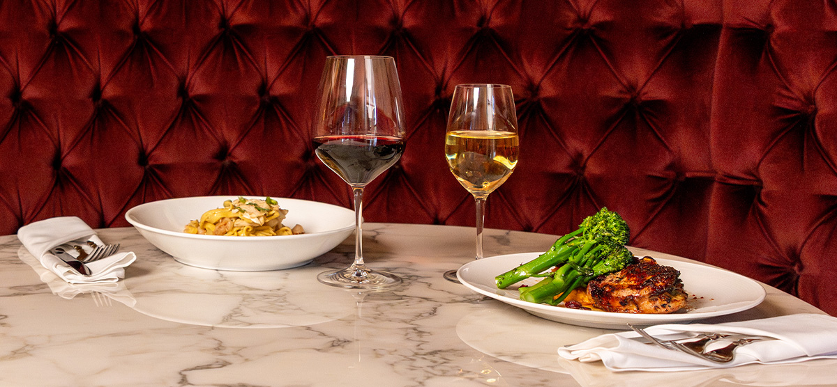 Bowl of pasta with red wine and plate of chicken with white wine. 