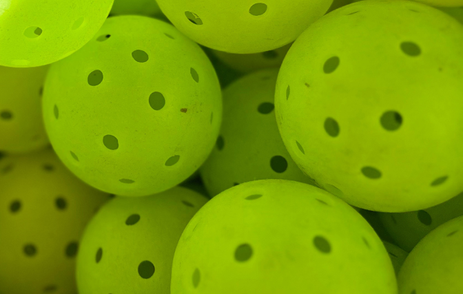 Close-up of many bright green, perforated pickleballs.