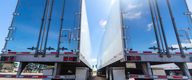 Two semi trailer trucks from behind on sunny day