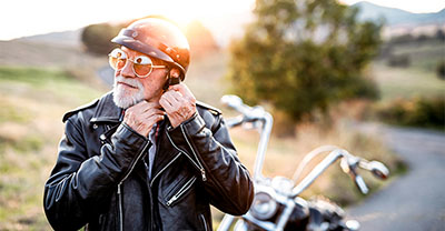 A senior man with motorcycle in countryside, putting on a helmet.