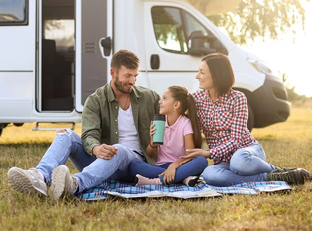a family sitting in the grass next to their motor home