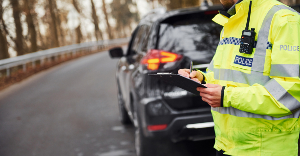 Police officer writing on clipboard behind parked car