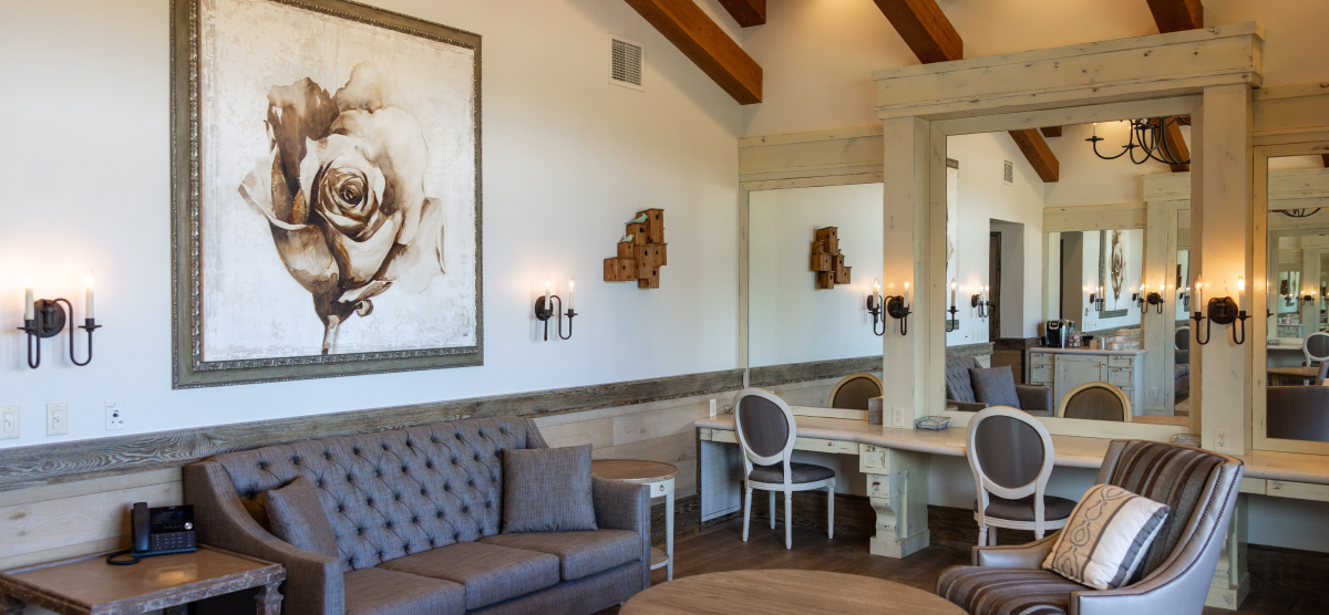 Seating area with a couch and chairs with three stations behind with a chairs and large mirrors.