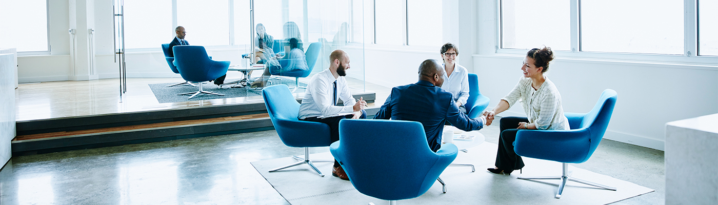 Business professionals in a modern office lounge, with two people shaking hands.