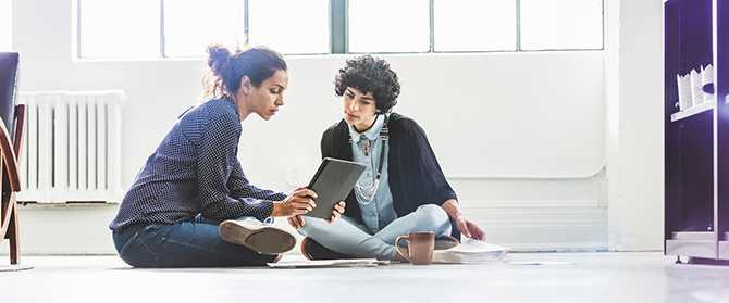 Two people sitting on the floor looking at a tablet