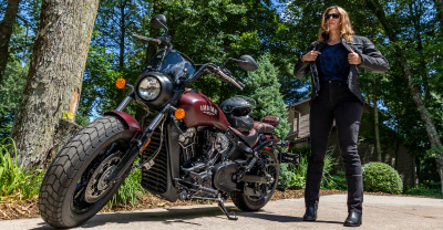 Biker woman putting on jacket next to parked motorcycle