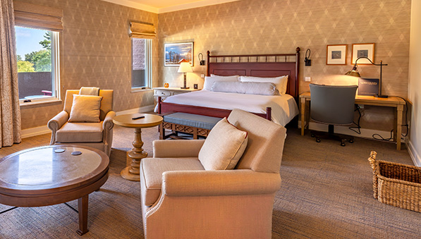 Hotel room with a king size bed, two chairs with coffee table, and a desk in muted tones. 