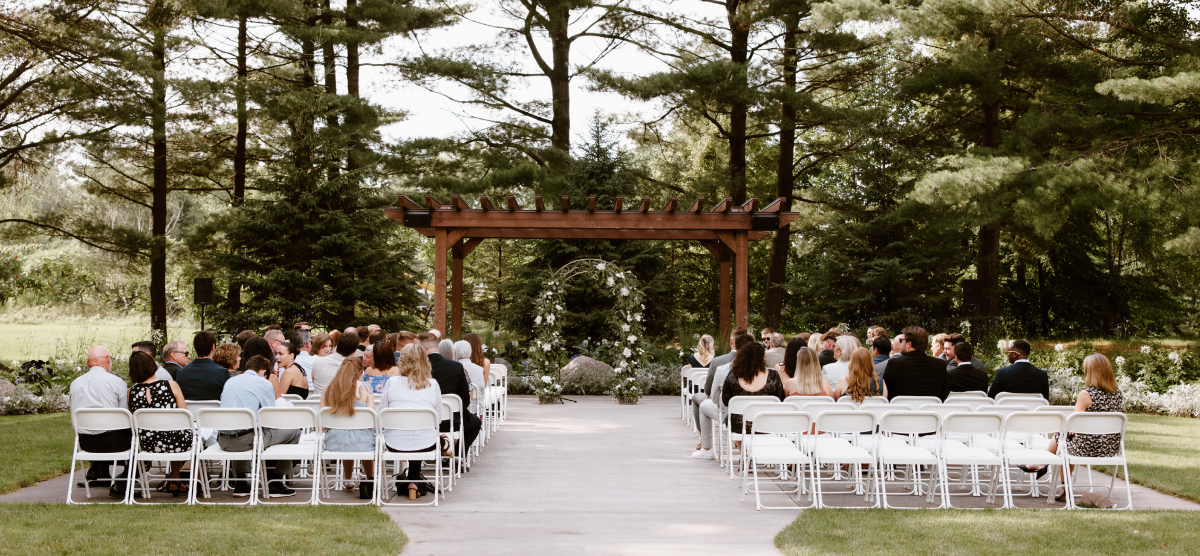 Guests seated at an outdoor wedding ceremony with a floral archway under a pergola.