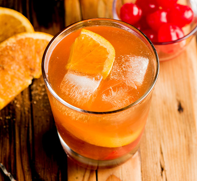 Cocktail with an orange slice next to a bowl of cherries