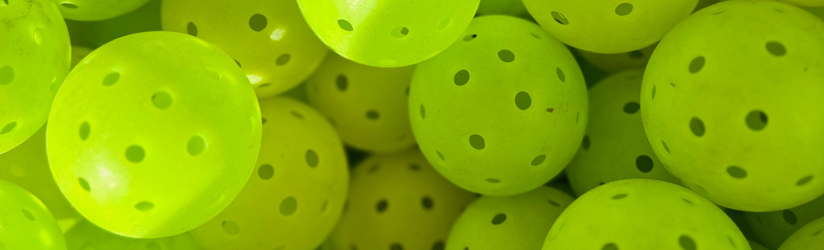 Close-up of many bright green, perforated pickleballs.