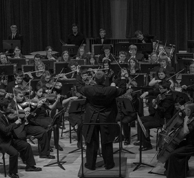 Black and white image of a youth orchestra playing on stage. 