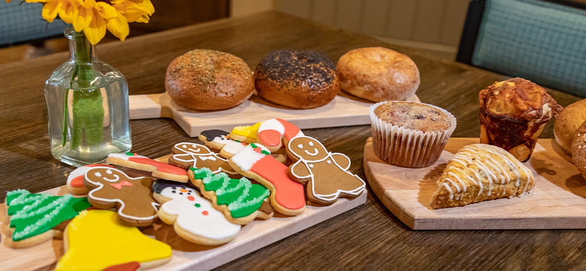 Holiday cookies and other bakery goods on a wooden tray next to a sunflower in a vase