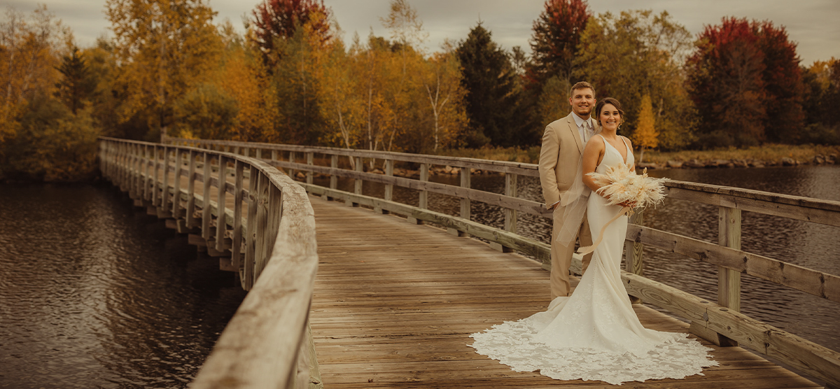 Groom and bride holding a wedding bouquet on a bridge during fall at SentryWorld