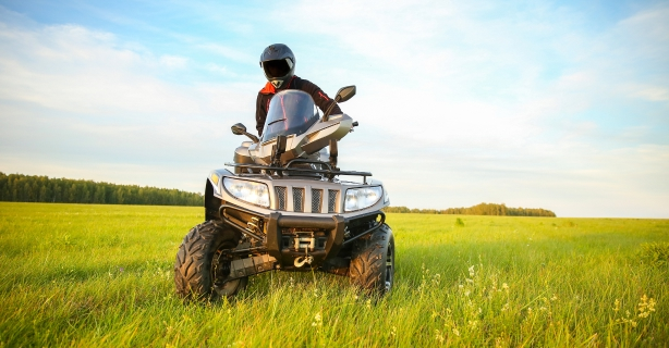 Person wearing a helmet and riding an ATV in an open grass area. 