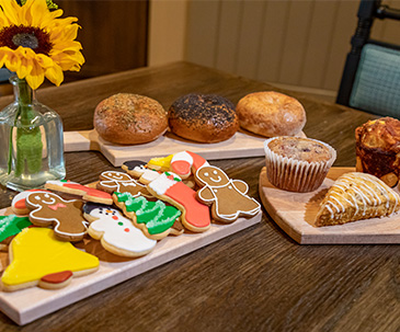 Holiday cookies and other bakery goods on a wooden tray next to a sunflower in a vase