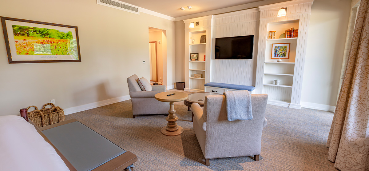 carousel-accessible-golf-view-executive-junior-suite-2-1200x556 King bed with two chairs facing a tv with a bench below.