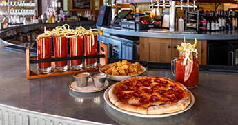 PJs bloody mary flight, cheese curds, and pepperoni pizza sitting on the PJs round bar.