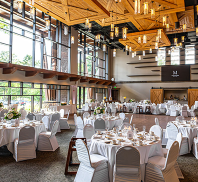 hero-wedding-venue-396x364 Atrium room with white tables and chairs and a wall of windows behind.