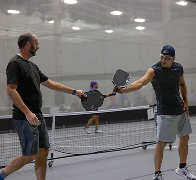 Two male pickleball players tapping paddles. 
