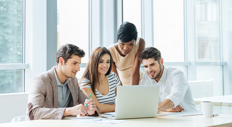 Four people in an office huddled around a laptop computer