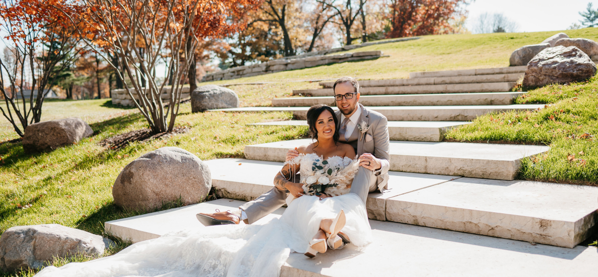 Bride and groom sit on stone steps outdoors, smiling at the camera.