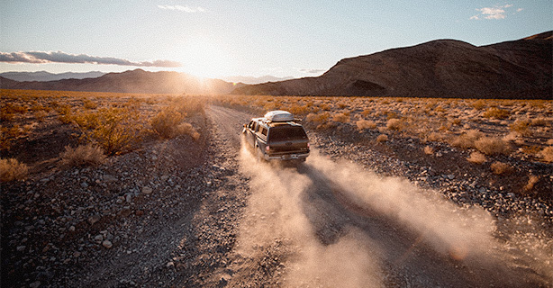 Vehicle driving down a dusty road towards the sunset