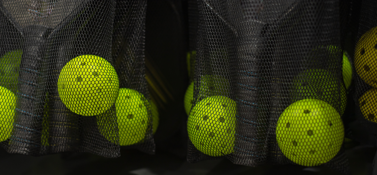 Bright yellow pickleballs in black mesh bags.